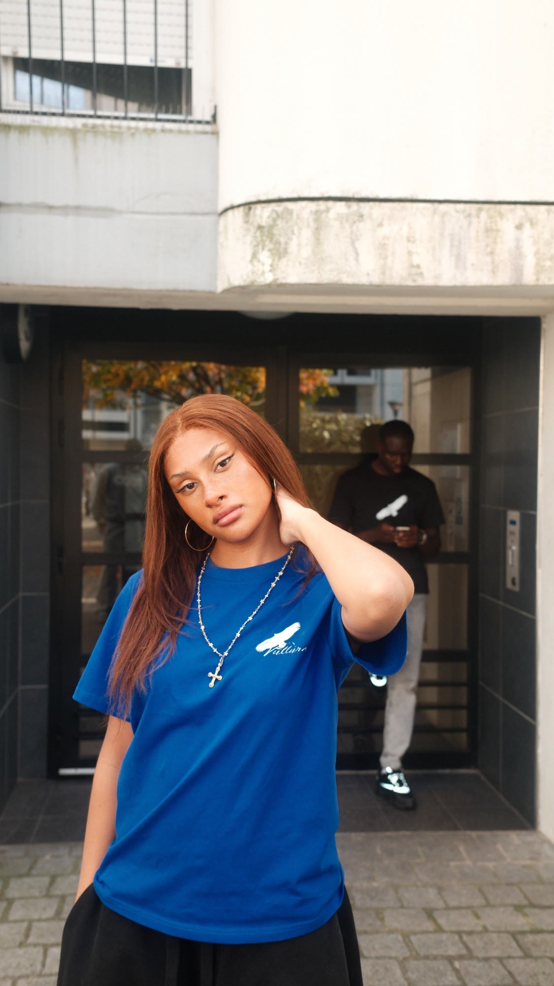 Jeune femme en tee bleu Vultura devant un hall d'immeuble