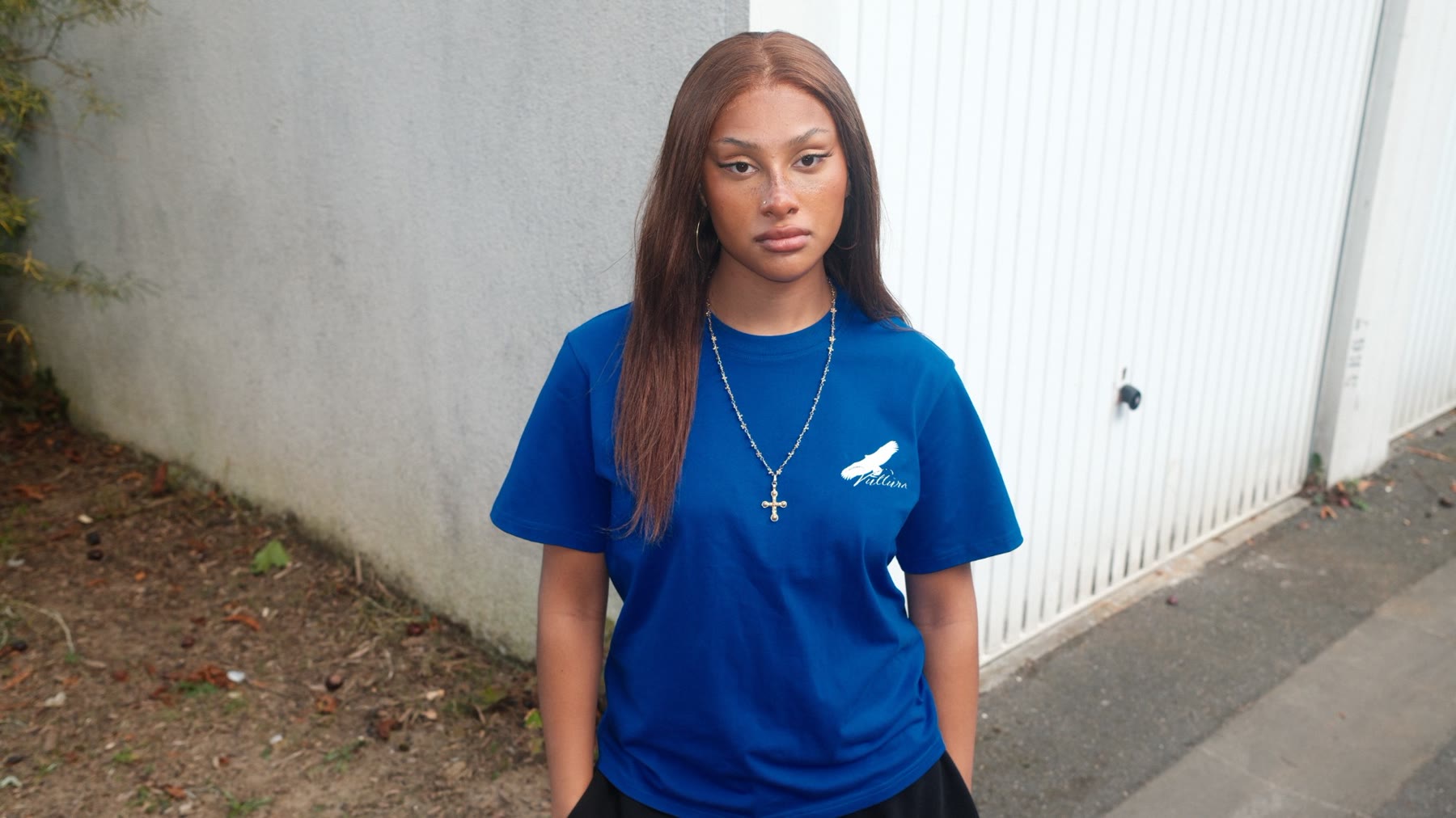Jeune femme en tee bleu Vultura devant un mur gris