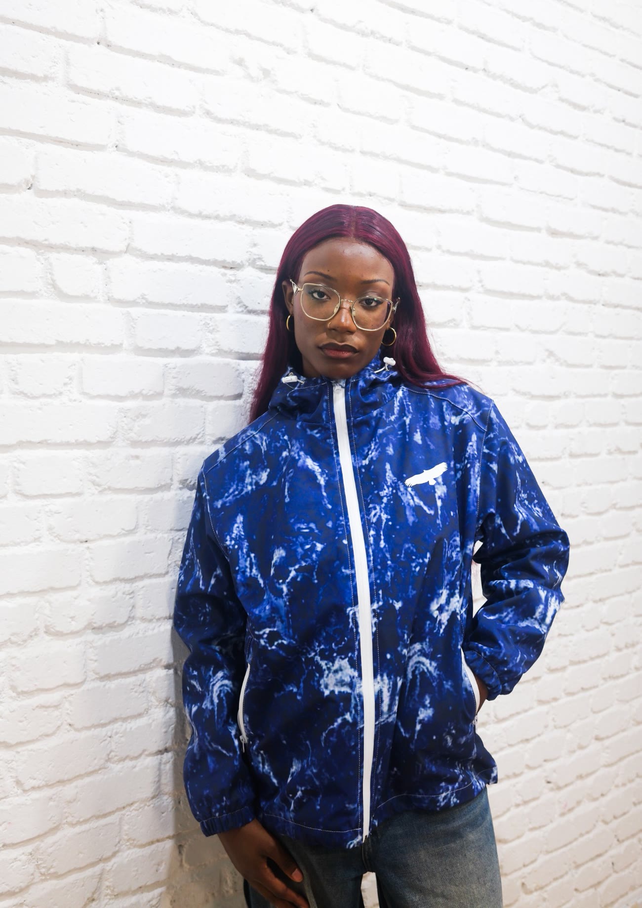 Jeune femme en coupe-vent Windbreaker Blue contre un mur de briques blanches