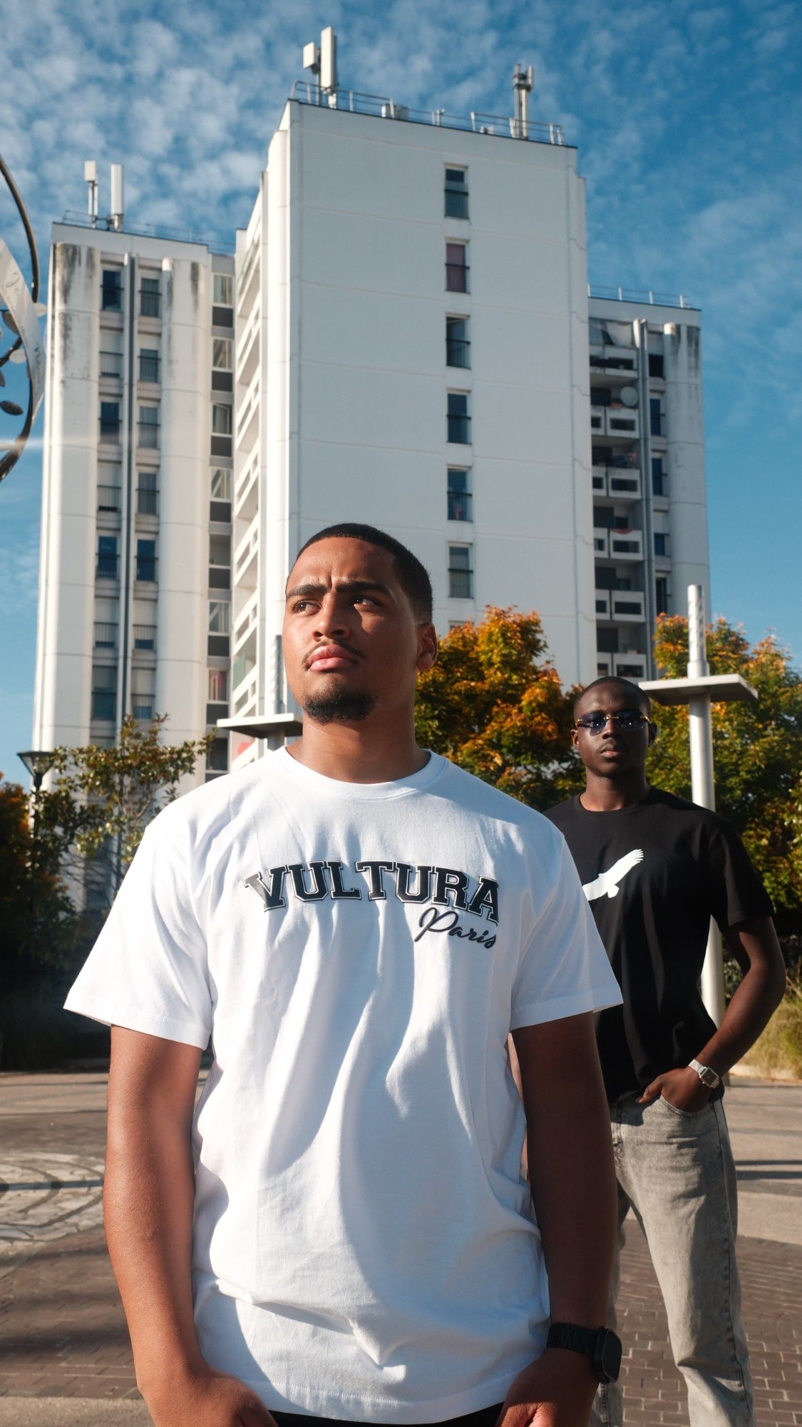 Deux jeunes hommes en tees Vultura devant une tour blanche